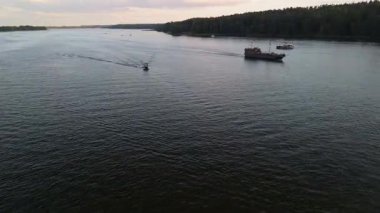 Mikolajki, Polonya, 9 Ağustos 2024: Teknelerin hareket ettiği muhteşem bir göl manzarası. Güneş ağaçların ardından batarken küçük bir motorlu tekne daha büyük tur gemilerinin yanından hızla geçiyor.