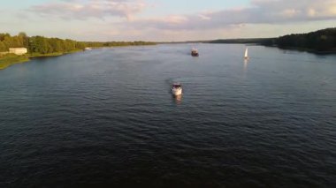 Mikolajki, Polonya, 9 Ağustos 2024: Gün batımında sakin bir nehirde seyreden motorlu botların sakin manzarası, yemyeşil bankalar ve arka planda uzak gemiler