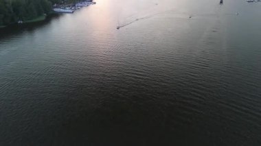 Mikolajki, Polonya, 9 Ağustos 2024: Gün batımında sakin sularda yüzen teknelerin manzarası, kıyı boyunca demirlemiş yatlar görülebilirken yüzeyde dalgalanmalar yaratıyor.