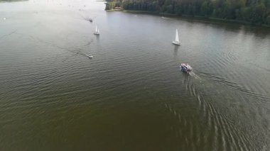 Mikolajki, Polonya, 9 Ağustos 2024: Sakin bir yaz öğleden sonrasında geniş bir göl boyunca ilerleyen yelkenli ve yolcu botlarının havadan çekimi