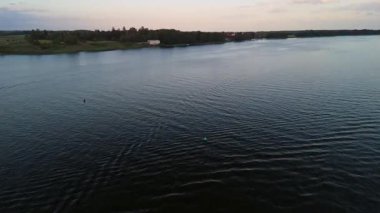 Mikolajkiat alacakaranlığında hafif göl dalgalanmaları, görünür şamandıralar ve suda yansıyan yumuşak pastel gökyüzü..