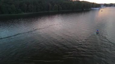 Mikolajki 'deki sakin göl sularından geçen küçük bir teknenin hava görüntüsü alacakaranlıkta hafif dalgalanmalar bırakıyor..