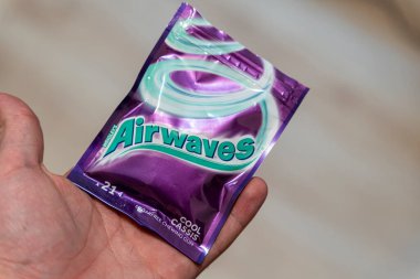 Varşova Polonya - 5 Aralık 2025: sakız çiğneyen bir radyo dalgası paketi tutan bir el. Canlı mor ve yeşil renkler markanın kimliğini ve ambalaj tasarımını pazarlama için ideal hale getiriyor..