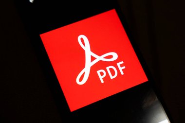 Varşova Polonya - 4 Aralık 2025: Kırmızı zemin üzerinde beyaz PDF logosunu gösteren akıllı telefonların yakın çekim görüntüsü. Görüntü, dijital belgeler ve modern iletişimi vurguluyor.