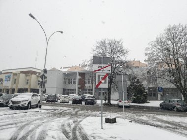 Rzeszow Polonya - 21 Kasım 2025: Park halindeki arabalarla sokağa yağan karı ve sınırlandırılmış yol ulaşımını gösteren bir tabelayı gösteren bir kış sahnesi.