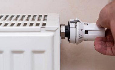 Beyaz bir radyatörün termostat valfini ayarlayan bir el kış boyunca ev ısısını ve konforu en uygun sıcaklık düzenlemesini sağlar..