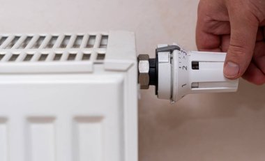 Beyaz bir radyatörün termostat düğmesini ayarlayan ve kış veya soğuk havalarda ısınmak için ısı kontrolüne odaklanan bir kişinin yakın çekimi.