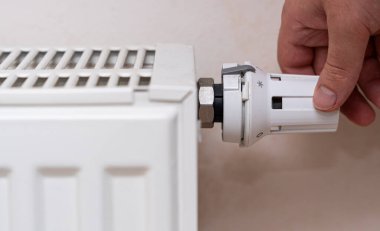 Isıtıcı kapakçığı evde ayarlayan ve sıcak bir ev ortamında sıcaklık kontrolüne odaklanan bir kişi. Soğuk aylarda konfor sağlamak.