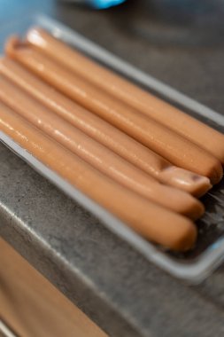 A close-up of several sausages placed in a clear plastic tray on a dark countertop. These sausages are ready for cooking or serving at a meal showcasing their smooth texture.