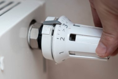 Ev ortamında radyatör ısıtma sisteminin ısı kontrolünü ayarlayan bir el. Bu görüntü iklim kontrolü ve enerji verimliliğinin önemini yansıtır..