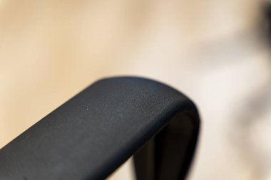 Ergonomik tasarımı gösteren siyah desenli bir sandalyenin kol bandının yakın çekimi. Sessiz arka plan, konfor ve modern mobilya estetiğine odaklanmayı vurguluyor.
