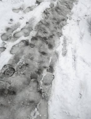 Footprints and tire tracks on a snow-covered road show winter conditions. The scene captures the hustle of daily life amidst cold weather. Ideal for winter-themed projects.