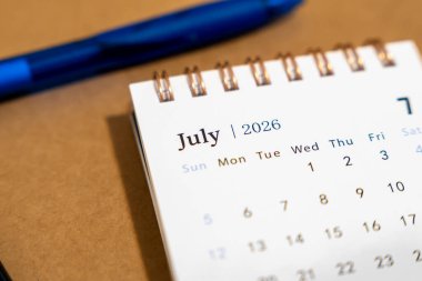 Temmuz 2026 'yı gösteren bir takvim sayfasının yakınında mavi bir kalem var. Sahne, bir aylık kişisel planlamayı yansıtan organizasyon ve zaman yönetimini iletir..