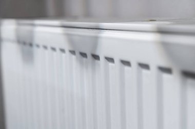 Beyaz bir radyatörün, deseni ve tasarımını ön plana çıkaran yakın görüntüsü. Dikey çizgilere ve gölgelere odaklanmak ev veya ofis ayarları için ilginç bir görsel öğe oluşturur.