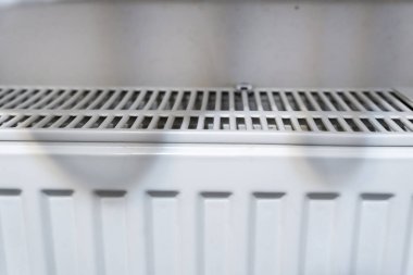 Tarafsız bir duvara karşı ızgara kapaklı beyaz radyatör ısıtıcısı. Bu resim, iç tasarım veya bakım bağlamları için uygun evlerdeki ortak bir ısıtma elementini vurgular.