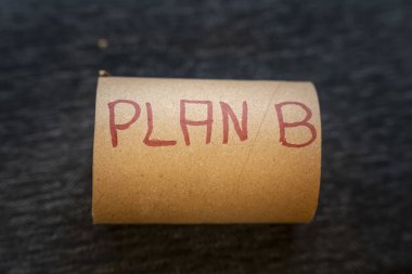 El yazısıyla yazılmış PLAN B metninin bulunduğu kahverengi bir kağıt tüp, planlama ve karar verme senaryolarıyla ilgili alternatif stratejiler veya çözümler sunuyordu.