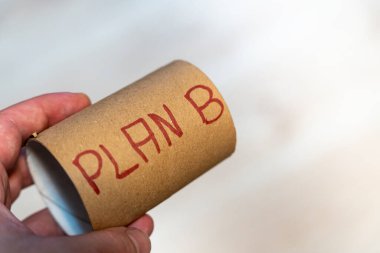 Bir kişi, alternatif stratejileri ya da yedek planları sembolize eden üzerinde Plan B yazan karton bir tüp tutuyor. Hafif arkaplan, konseptin basitliğini ve odaklanmasını vurgular..