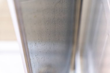 Banyo ortamında buharın etkilerini vurgulayan nem damlacıklarıyla kaplı cam duş kapısının yakın çekimi. Temizlik, rahatlama ve hijyen için ideal..