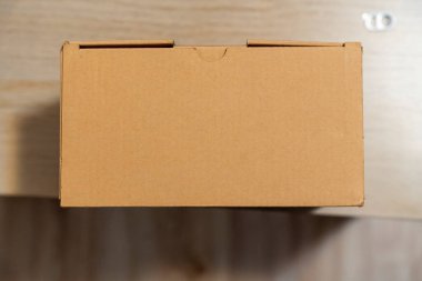 Sade kahverengi bir karton kutu, basitlik ve işlevselliği gösteren ahşap bir masanın üzerine yerleştirilir. Paketleme veya depolama çözümleri için ideal.