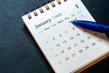 Takvimin yakın çekim görüntüsü Ocak 12026 'ya kadar açıldı ve yanında mavi bir kalem duruyor. Tarih, planlama ve organizasyonu gösteren yeni bir yılın başlangıcını vurguluyor.