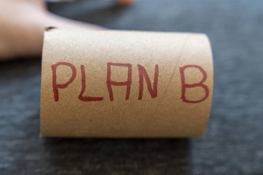 Karton rulo üzerindeki el yazısı PLAN B, olasılık planlamasını ve alternatif çözümleri sembolize eder. Tarafsız ayar çeşitli bağlamlarda hazırlanmanın önemini vurgular.
