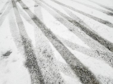 Taze kardaki lastik izleri ve ayak izleri, kış manzarasında beyaz kar ve aşağıdaki daha koyu yüzeyler arasındaki zıtlığı gösteren bir desen oluşturur..