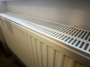 Isıtma sağlayan bir odaya kurulmuş modern beyaz bir radyatörün yakın çekimi. Kapağın ince çizgileri ve ızgara deseni iç sıcaklık için verimlilik ve çağdaş tasarım öneriyor..