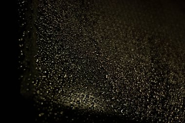 Su damlacıklarının koyu bir yüzeydeki yakın görüntüsü yoğunlaşmayı gösteriyor. Damlacıklar, görsel estetiği yansıtan ışık yansıtan soyut bir tasarım yaratıyor..