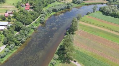 Tarlaların yanında akan bir nehrin yüksek hava manzarası ve yavaş su hareketli dağınık binalar ve kırsal bölgelerde görülebilen çeşitli arazi şekilleri.