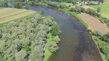 Görünür akım ve yoğun yeşil bitki örtüsü ile yama arazisinden akan hafif kıvrımlı bir nehrin havadan görünüşü parlak gün ışığı altında kıyıları kaplıyor.