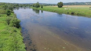 Yeşil bitki örtüsünün içinden akan sakin bir nehrin havadan görünüşü yumuşak yüzey hareketi ve kırsal bir alanda açık gün ışığı altında yansımaları.