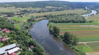 Yama alanları ve yeşil bankalar temiz yaz güneşi altında durağan su hareketlerini gösteren ekili tarlalardan akan dolambaçlı bir nehrin havadan görünüşü
