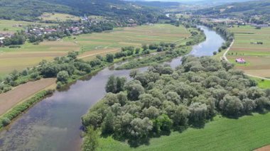 Yamalı tarım arazilerinden geçen dolambaçlı bir nehrin yüksek hava manzarası ve berrak yaz güneşi altında durgun su hareketleri olan yeşil bankalar.