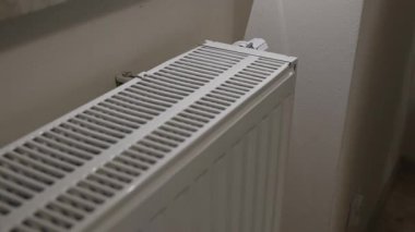 Ev kaloriferini yakından gören bir kişi, el ile üst ızgarayı ayarlar. Ev ortamında ince bir hareket ve kapalı ısıtma ekipmanı detaylarını gösterir.