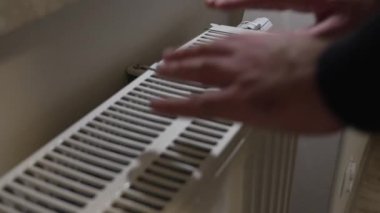 Sıcak bir radyatör ızgarasında el ele tutuşurken yakın çekim. İç mekandaki ısıtma performansını test ederken hafif bir hareket gösteriyor.