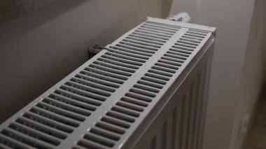 Ev içi ısıtma kullanımı ve kişisel enerji tüketimini gösteren ısı çıkışını kontrol etmek için radyatör ızgarasına dokunan bir elin yakın görüntüsü