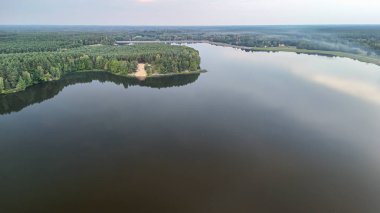Yoğun ormanlarla çevrili sakin bir göl, berrak bir gökyüzü altında doğal güzellikleri ve barışçıl manzaraları sergiliyor. Doğa temalı projeler veya rahatlama için ideal.