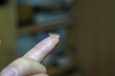 Parmak ucunda lens tutan bir kişi lensin boyutunu ve şeffaflığını gösterir. Bu resim, reklamlar veya eğitim kullanımı için uygun kişisel bakım ve göz sağlığını göstermektedir..
