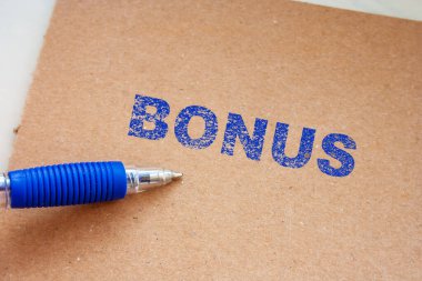 Kahverengi bir arka planda BONUS 'un mavi kalemle birlikte el yazısıyla yazılmış olduğunu belirten bir metin. Bu imaj, çeşitli işletmeler için ödülleri ve terfileri temsil ediyor..