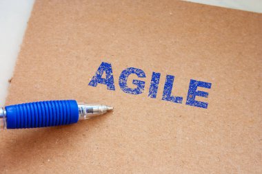 Kahverengi desenli kağıt zemin üzerinde kalın mavi mürekkeple yazılmış AGILE el yazısı bir pazarlama kavramsal atmosferi sağlıyor. İş ve yenilik temaları için ideal.