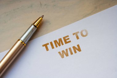 Beyaz bir kağıtta el yazısıyla yazılmış bir notta Time to WIN yazıyor ve yanında da lüks bir kalem var. Bu görüntü kişisel ya da iş amaçlarına uygun motivasyon ve başarıyı anımsatıyor.