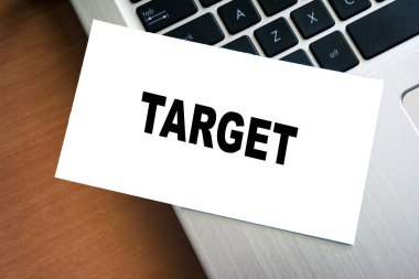 El yazısıyla yazılmış bir kelime TARGet boş beyaz bir sayfa üzerine dizüstü bilgisayarın arka planında hedefleri sembolize eden ve iş veya özel hayata odaklanan bir kağıt..