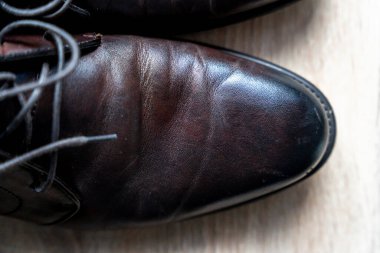 Ahşap arka planda cilalanmış kahverengi deri ayakkabıların yakın görüntüsü. Bu ayakkabılar, el işçiliği ve stili vurgulayan resmi durumlar için klasik bir tasarım özelliğidir..