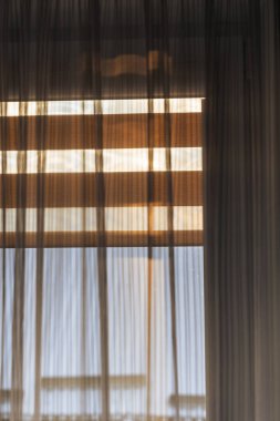 Saf perdelerden süzülen yumuşak güneş ışığı, gündüz vakti ev ortamında sakin bir atmosfer yaratan rahat bir iç mekanın güzelliğini vurgular..