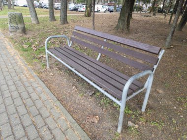 Rzeszow Polonya - 19 Aralık 2025: Dağınık kuru yapraklı bir orman bölgesinde bulunan kahverengi ahşap park bankı, ziyaretçilere kamusal alanda dinlenme yeri sağlıyor.