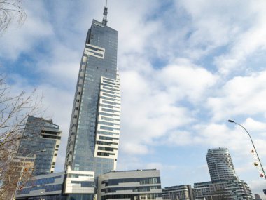 Rzeszow Polonya - 19 Aralık 2025: Mavi gökyüzü ve mevsimsel yeşillikler arasında çağdaş mimariyi gözler önüne seren canlı kentsel bir gökdelende modern gökdelen.