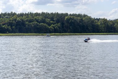 Mikolajki Polonya - 29 Eylül 2024: Güneşli bir günde canlı bir açık hava eğlence sahnesi sergilenen yemyeşil bir göl üzerinde iki tekne geziniyor.