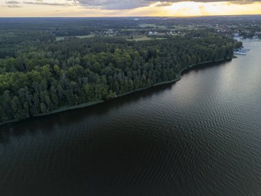 Yoğun ormanlarla çevrili sakin bir göl ve günbatımında arka planda büyüleyici bir köy doğa ve manzara projeleri için ideal..