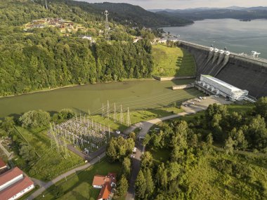 Solina Poland - 29 Haziran 2024: Solina Barajı 'nın çevresi yemyeşil sularla çevrili ve göl kenarındaki hidroelektrik santrali ve iletim hatlarını gösteren hava manzarası.