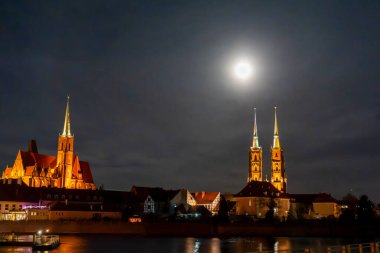 Aydınlatılmış Wroclaw gökyüzünde yükselen belirgin kuleler de dahil olmak üzere gotik mimari içerikli gökdelenler büyüleyici bir şehir manzarası yaratıyor..